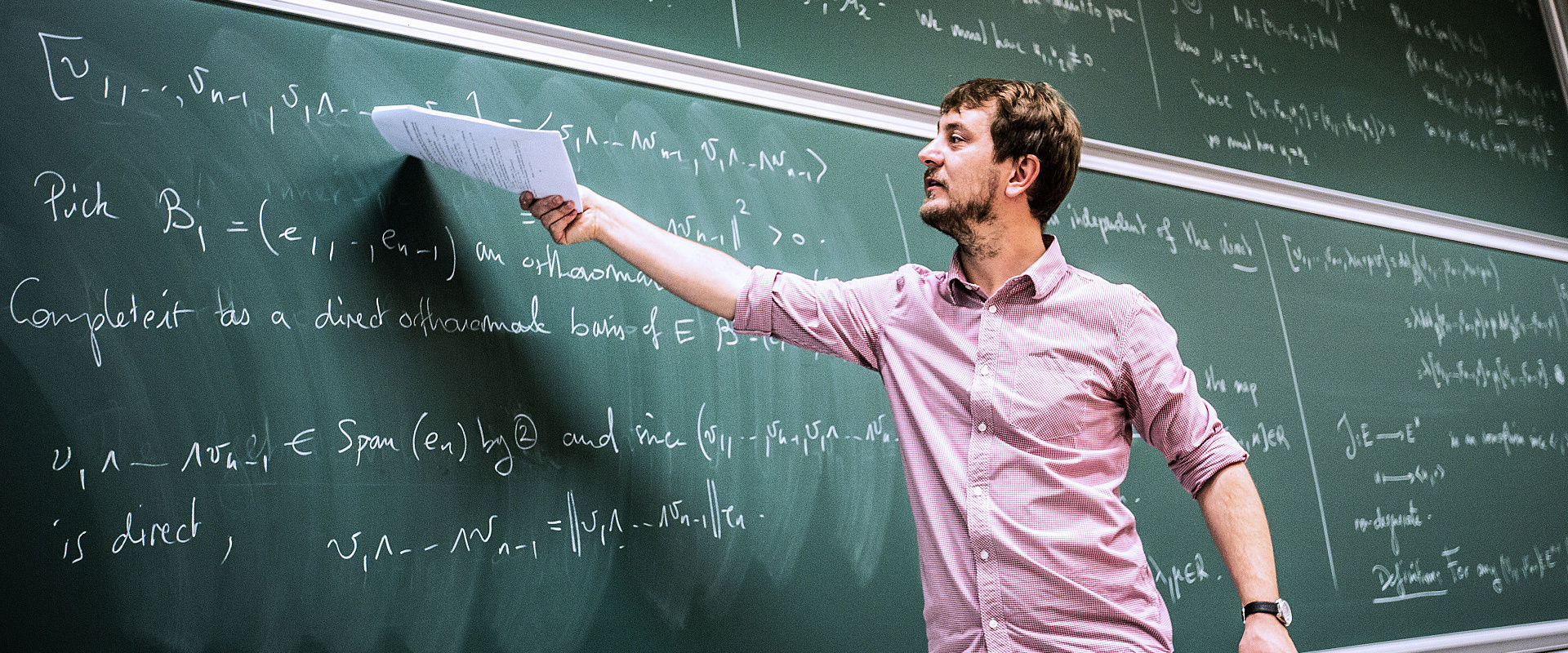Classroom setting with a teacher at a whiteboard and students at desks.